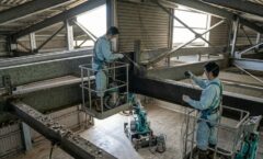 倉庫の高所で、プロの技術者が高所作業車を使いハトのフンを強力清掃し、防鳥ネットを設置している。徹底した再発防止施工の様子。