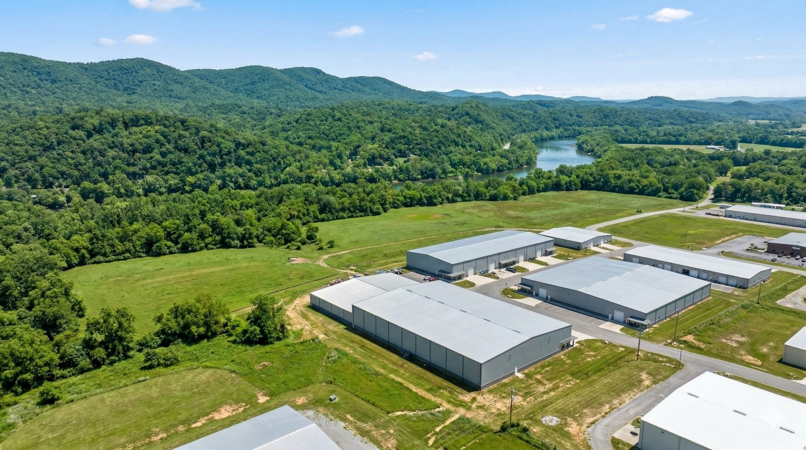 福岡県那珂川市の豊かな自然環境（山、川、緑）と、それに隣接する物流倉庫街の空撮写真。ハトが住み着きやすい環境であることを示す。
