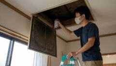 自宅の天井裏の点検口から、くん煙タイプのネズミ忌避剤を設置しようとする日本人男性。