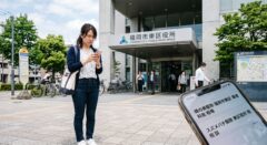 福岡市東区役所の前で、蜂の巣駆除について不安げにスマートフォンで検索する日本人の女性