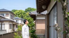 福岡市東区の住宅で、白い服を着た日本人の男性が安全な距離から自宅の軒下にできたハチの巣を静かに確認する様子
