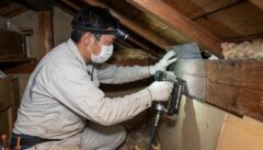 日本の住宅の屋根裏で、専門の技術者が金網と専用工具を使って、イタチの再侵入を防ぐために隙間を完全に塞ぐ封鎖工事を行っている様子。