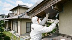 佐賀市の住宅で、防護服を着た専門業者がコウモリの侵入経路（軒下の隙間）を金網とコーキング剤で完全に封鎖する作業
