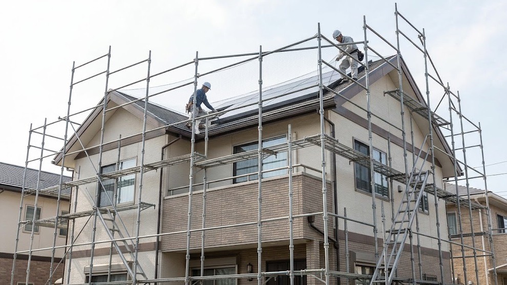 小倉の戸建て住宅で、足場を組んで太陽光パネル周辺にハト対策のネットを設置する日本人作業員。