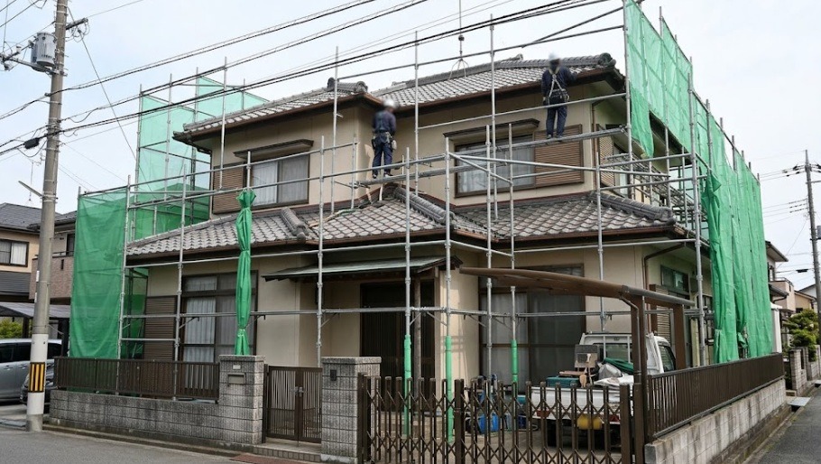 高所の軒下や屋根でのコウモリ駆除・侵入口封鎖工事のために、2階建ての戸建て住宅の周囲に設置された金属製の仮設足場と安全ネットの様子